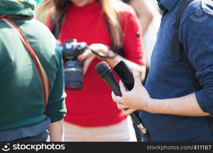 Reporter at media event holding microphone, blurred female photographer in the background