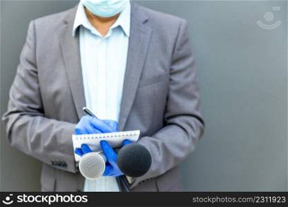 Reporter wearing protective gloves and face mask against coronavirus COVID-19 disease holding microphone reporting during virus pandemic