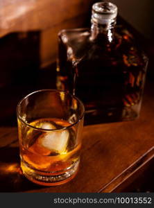 Reposado tequila Old Fashioned cocktail sitting on a wooden desk near a decanter.