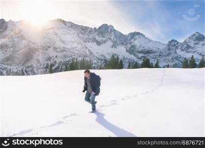 Representative image of the winter season, with snowy mountain peaks, fir forest and a man wandering through a thick layer of snow, in Ehrwald, Austria.