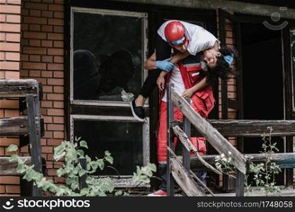 Rescue worker carrying disaster victim out of damaged house
