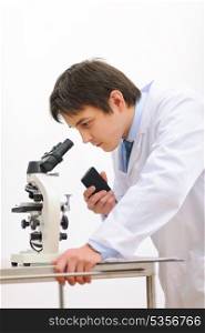 Researcher looking in microscope and making notes on voice recorder