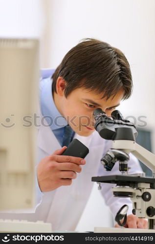 Researcher looking in microscope and making notes on voice recorder in laboratory