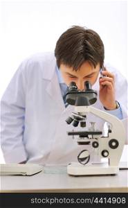 Researcher looking in microscope and speaking mobile in medical laboratory