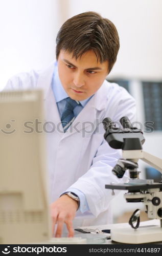 Researcher working in medical laboratory using microscope and computer