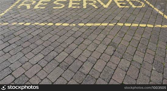Reserved parking sign painted in yellow on stone pavement. Reserved parking sign