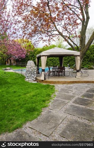 Residential backyard with gazebo, deck, stone patio and swimming pool