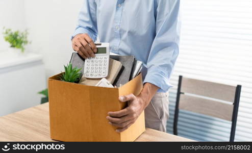 Resignation Concept The man in light blue shirt standing at the desk and putting the calculator and other stuff into the box.