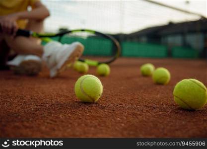 Rest after game shot with focus on balls scattered across playing field and relaxed tennis player sitting on floor. Rest after game shot with focus on balls scattered across playing field