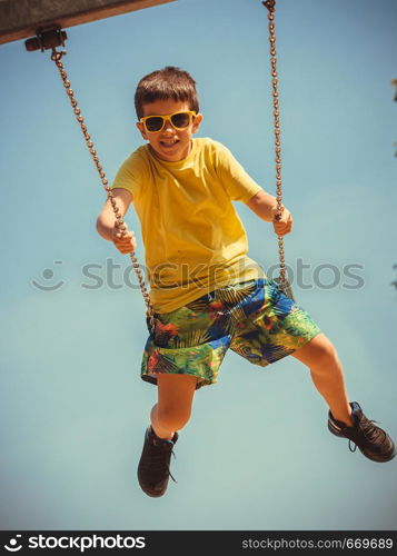 Rest and relax for children. Little boy in sunglasses resting swinging outdoor. Adorable child having fun playing in playground.. Boy playing swinging by swing-set.