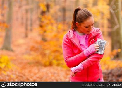 Rest and relax. Young attractive sporty girl with mobile phone smartphone on her arm with headphones listening music.. Sporty girl rest in forest listening music.