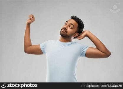rest, bedtime and people concept - indian man stretching over grey background. indian man stretching over grey background