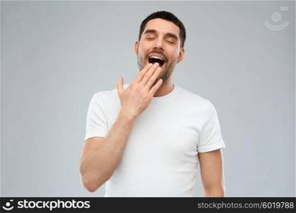 rest, bedtime and people concept - tired yawning man over gray background
