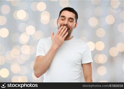 rest, bedtime and people concept - tired yawning man over holidays lights background