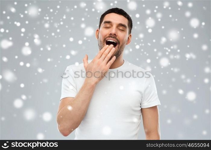 rest, bedtime, winter, christmas and people concept - tired yawning man over snow on gray background