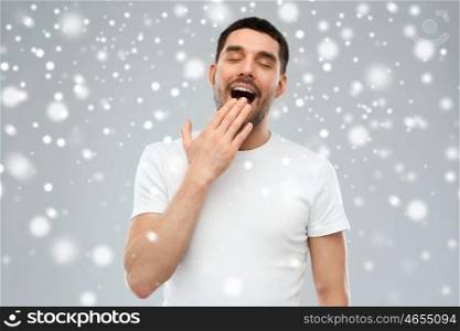 rest, bedtime, winter, christmas and people concept - tired yawning man over snow on gray background