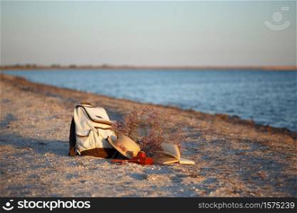 rest by the sea. backpack, hat, book, camera and bouquet on the background of the sea On the Sunset