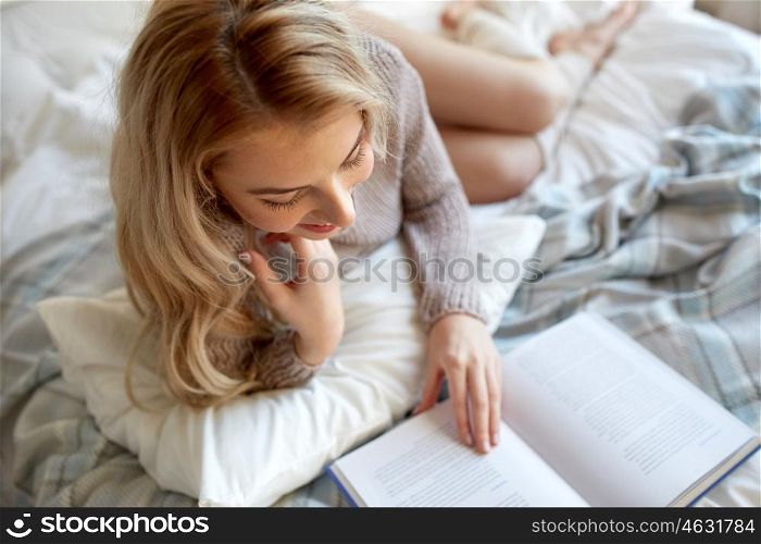 rest, comfort, leisure and people concept - close up of happy young woman reading book in bed at home bedroom