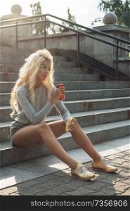 Rest in street, outdoor, people and leisure concept - beauty blonde young woman sitting on outdoor and eating. beauty blonde young woman sitting on outdoor and eating