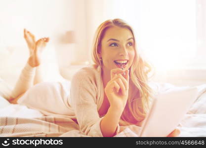 rest, inspiration, creativity, comfort and people concept - happy young woman with pen and notebook dreaming in bed at home bedroom