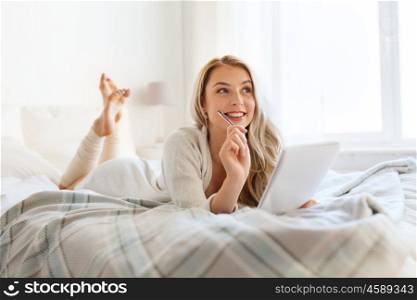 rest, inspiration, creativity, comfort and people concept - happy young woman with pen and notebook dreaming in bed at home bedroom