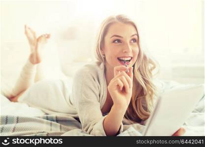 rest, inspiration, creativity, comfort and people concept - happy young woman with pen and notebook dreaming in bed at home bedroom. happy young woman with notebook in bed at home