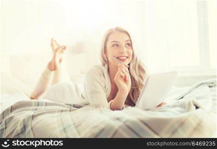 rest, inspiration, creativity, comfort and people concept - happy young woman with pen and notebook dreaming in bed at home bedroom. happy young woman with notebook in bed at home
