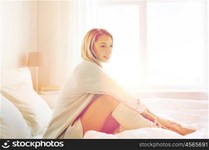 rest, sleeping, comfort and people concept - happy young woman sitting in bed at home bedroom