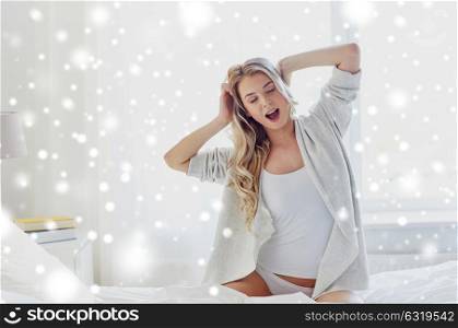 rest, sleeping, comfort and people concept - happy young woman stretching and yawning in bed at home bedroom over snow. young woman stretching in bed at home bedroom
