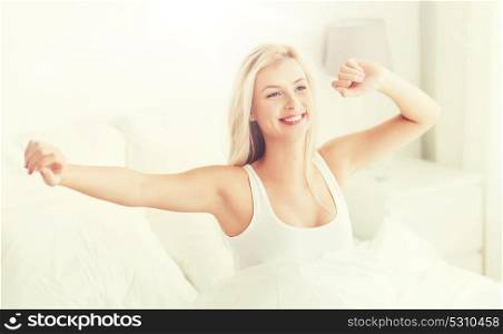 rest, sleeping, comfort and people concept - happy young woman stretching in bed after waking up at home bedroom. young woman stretching in bed after waking up