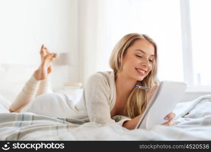 rest, sleeping, comfort and people concept - happy young woman with pen and notebook writing in bed at home bedroom