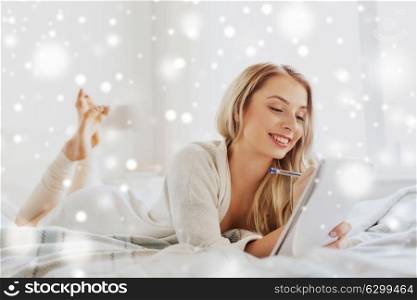 rest, sleeping, comfort and people concept - happy young woman with pen and notebook writing in bed at home bedroom over snow. happy young woman with notebook in bed at home