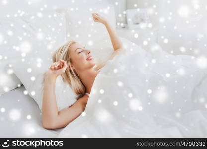 rest, sleeping, comfort and people concept - young woman stretching in bed at home bedroom over snow