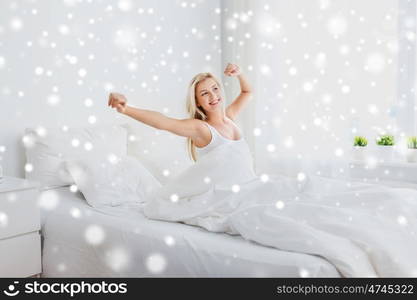 rest, sleeping, comfort and people concept - young woman stretching in bed at home bedroom over snow