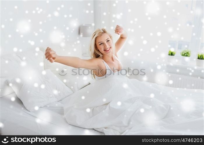 rest, sleeping, comfort and people concept - young woman stretching in bed at home bedroom over snow