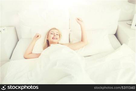 rest, sleeping, comfort and people concept - young woman stretching in bed at home bedroom. young woman stretching in bed at home bedroom