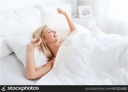 rest, sleeping, comfort and people concept - young woman stretching in bed at home bedroom