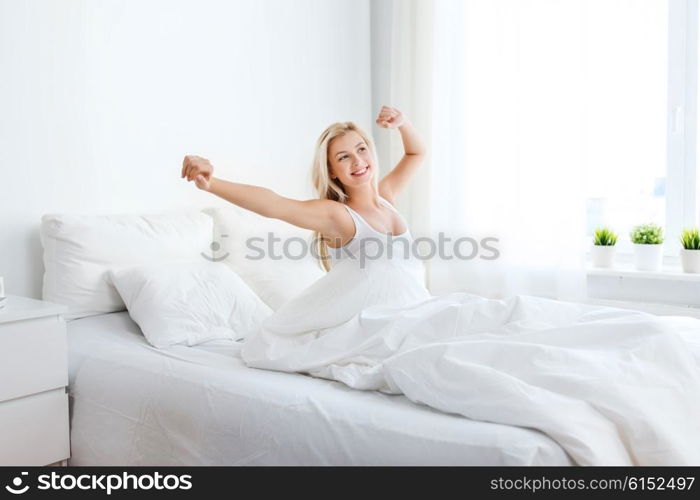 rest, sleeping, comfort and people concept - young woman stretching in bed at home bedroom