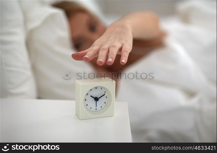 rest, sleeping, time and people concept - close up of young woman switching off alarm clock in bed at home bedroom