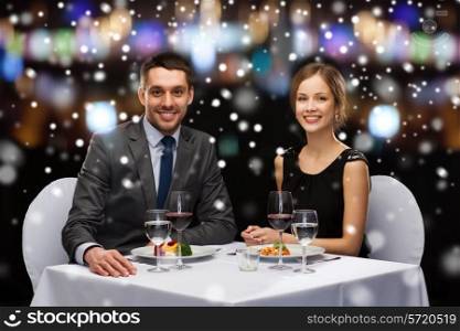 restaurant, christmas, holidays and people concept - smiling couple eating main course at restaurant over night lights background