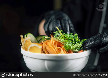 Restaurant cook decorating salad with arugula, black background, close up. Chef in Restaurant, Preparing Salad with Arugula