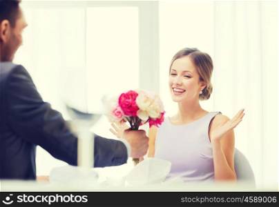 restaurant, couple and holiday concept - amazed woman recieving bouquet of flowers from husband or boyfriend at restaurant