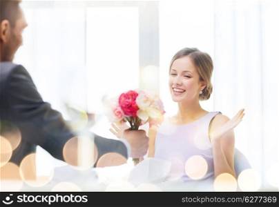 restaurant, couple and holiday concept - amazed woman recieving bouquet of flowers from husband or boyfriend at restaurant