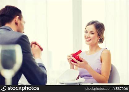 restaurant, couple and holiday concept - excited young woman looking at boyfriend with gift box at restaurant