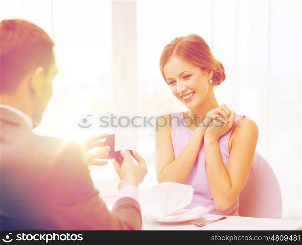 restaurant, couple and holiday concept - excited young woman looking at boyfriend with engagement ring at restaurant