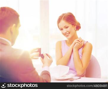 restaurant, couple and holiday concept - excited young woman looking at boyfriend with engagement ring at restaurant