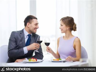 restaurant, couple and holiday concept - smiling couple with main course and red wine at restaurant