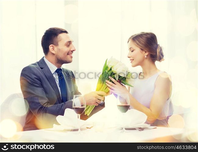 restaurant, couple and holiday concept - smiling man giving girlfriend or wife bouquet of flowers at restaurant