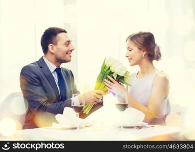 restaurant, couple and holiday concept - smiling man giving girlfriend or wife bouquet of flowers at restaurant