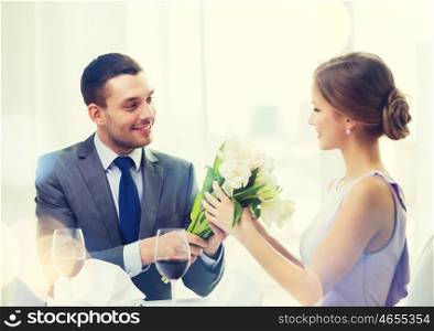 restaurant, couple and holiday concept - smiling man giving girlfriend or wife bouquet of flowers at restaurant